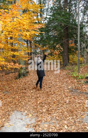 Rückansicht einer Reifen Frau, die Herbstblätter in die Luft wirft, Ontario, Kanada Stockfoto