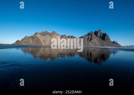 Vestrahorn und schwarzer Sandstrand spiegeln sich im Ozean, Stokksnes Peninsula, Island Stockfoto