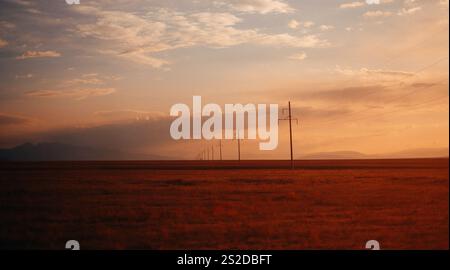 Reihe von Strommasten in der Wüstenlandschaft bei Sonnenuntergang, Kasachstan Stockfoto