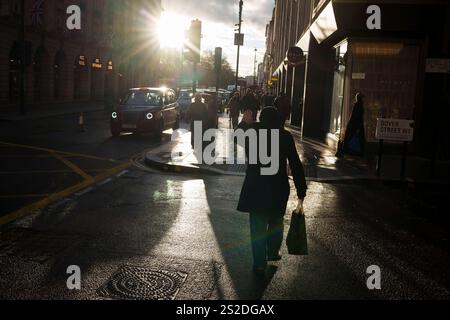 Ein Mann schützt seine Augen vor hellem Sonnenschein, während er am 7. Januar 2025 die Kreuzung Piccadilly Street und Dover Street in London überquert. Stockfoto