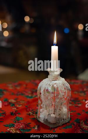 Eine brennende Paraffinkerze in einem Fläschchen auf einer roten Tischdecke. Paraffinstreifen. Stockfoto