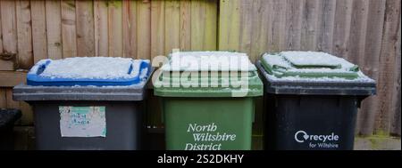 Drei schneebedeckte Recyclingbehälter im Freien stehen an einem Holzzaun in einem Wohngebiet Stockfoto