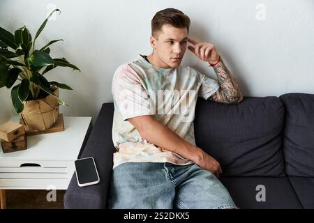 Gutaussehender junger Mann sitzt nachdenklich auf einer modernen Couch, umgeben von Grün. Stockfoto