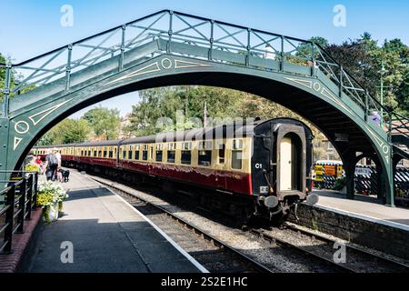 Alte Wagen mit Diesellokomotive, die unter der Fußgängerbrücke am Pickering Railway Station in North Yorkshire vorbeifahren Stockfoto
