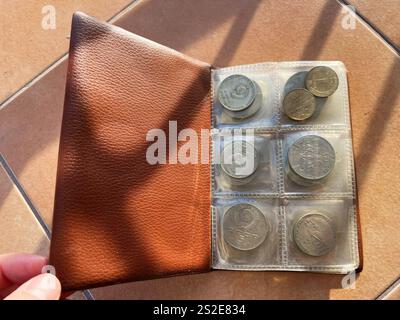 Kiew, Ukraine - 07. Januar 2025: Ein Bild einer braunen Münzbörse mit verschiedenen Münzen, die in transparenten Hüllen unter hellem Sonnenlicht ausgestellt sind. Stockfoto