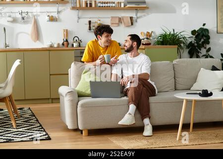 Zwei Männer teilen fröhliche Momente in einem stilvollen Apartment und genießen sich bei einem Kaffee Gesellschaft. Stockfoto