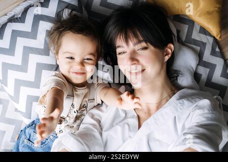 Eine fröhliche Mutter und ihr Kleinkind teilen einen glücklichen Moment, liegen auf einem Kissen mit Chevron-Muster. Fängt die Liebe der Familie, Wärme und authentische Verbundenheit ein Stockfoto