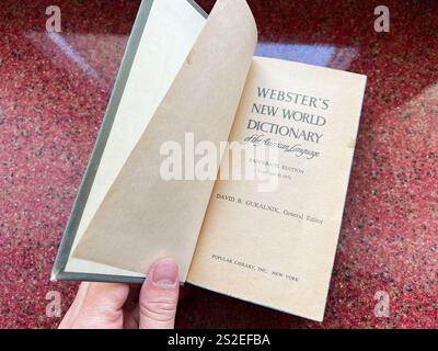 Kiew, Ukraine - 07. Januar 2025: Ein altes Webster's New World Dictionary wurde auf seiner Titelseite geöffnet und präsentiert sein empfindliches Papier. Gegen ein Rot gehalten, s Stockfoto