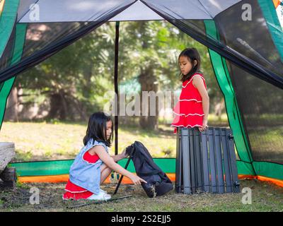 Zwei Schwestern helfen einander, an einem sonnigen Tag einen Tisch in der Natur zu schaffen. Familiencamping im Wald im Sommerurlaub Stockfoto