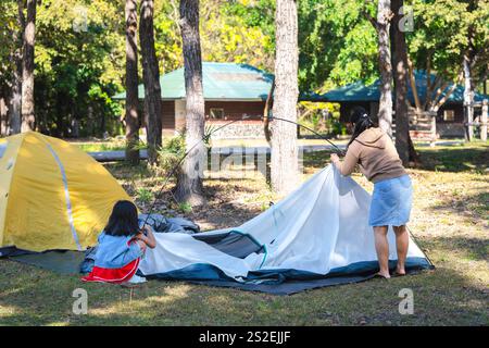 Mutter und Tochter helfen einander, an einem sonnigen Tag ein Zelt in der Natur aufzubauen. Familiencamping im Wald im Sommerurlaub Stockfoto