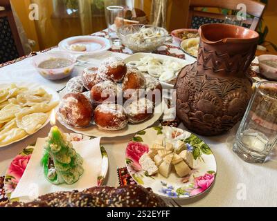 Ein wunderschön gestalteter Tisch mit traditionellen festlichen Speisen, Gebäck und einer dekorierten Keramikkanne. Eine Kerze in Baumform verleiht Wärme und Charme, perfekt Stockfoto