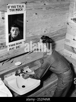 Ein US-Soldat schaut in den Waschzimmerspiegel mit einem Schild herum mit der Aufschrift "WENN DU ZU VIEL SPRICHST, KANN DIESER MANN STERBEN!". Ermutigung, keine Informationen zu verbreiten, die bei den Kriegsanstrengungen während des Zweiten Weltkriegs sensibel sein könnten. Camp Hood, Texas, 1943 Stockfoto