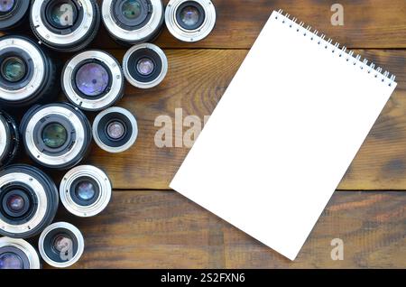 Mehrere Fotolinsen und ein weißes Notizbuch liegen auf braunem Holzhintergrund. Platz für Text Stockfoto