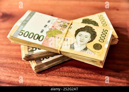 Drei Stapel koreanischer Banknoten auf einem Holztisch. Das Geld ist gelb und hat ein Frauengesicht drauf Stockfoto