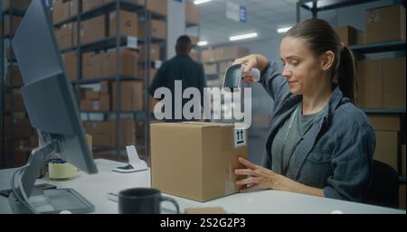 Logistikzentrum: Weibliche Postangestellte scannt Papppakete mit Barcode-Scanner, arbeitet am Computer. Kontrollkästchen für die Lieferung des Mitarbeiters im Sortierzentrum. Online-Shop-Lager. Stockfoto