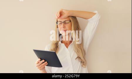 Müde überarbeitete, reife Angestellte, die mit einem Tablet-Computer arbeitet, unter Kopfschmerzen leidet, Frau, die im Home Office eine Brille trägt Stockfoto