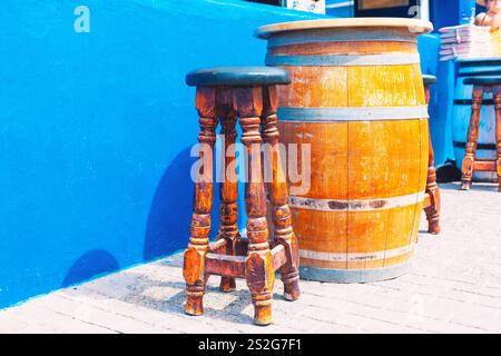 Rustikale Einrichtung mit einem Holzfass, der als Tisch umfunktioniert wird, und einem passenden Holzhocker, der an der blauen Wand aufgestellt ist. Das charmante Arrangement steht im Kontrast zu traditionellem Stockfoto
