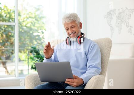 Senior-Mann mit Kopfhörern, der zu Hause Videoanrufe über Laptop führt Stockfoto