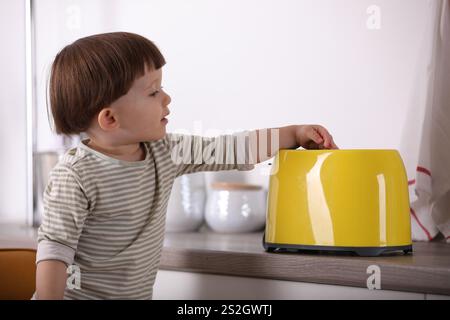 Kleiner Junge, der mit Toaster in der Küche spielt. Gefährliche Situation Stockfoto