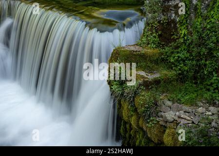 Ein Wasserfall stürzt über moosige Felsen, umgeben von üppigem Grün und Naturstein, und schafft eine ruhige und lebendige Naturszene Stockfoto