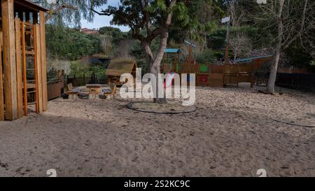 Ein Spielplatz mit Holzkonstruktionen, einer Rutsche und sandbedecktem Gelände, umgeben von Bäumen und natürlichem Grün in einer Außenumgebung. Stockfoto