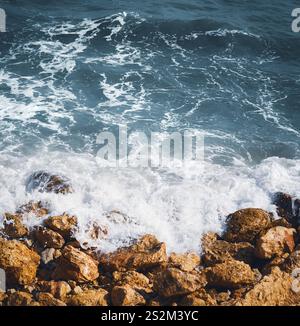 Tiefblaue Wasserwellen, die auf orangen Felsen krachen Stockfoto