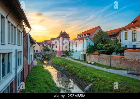 Ein malerischer Sonnenuntergang über einem bezaubernden Kanal in Donauworth, gesäumt von historischen Gebäuden. Bunte Häuser, eine kleine Brücke und üppiges Grün Stockfoto
