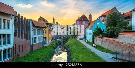 Ein malerischer Sonnenuntergang über einem bezaubernden Kanal in Donauworth, gesäumt von historischen Gebäuden. Bunte Häuser, eine kleine Brücke und üppiges Grün Stockfoto