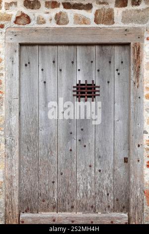 172 Mont-Saint-Michel: Alte, unbemalte, mit Nieten versehene Holztür mit Gitterspuckloch auf der Loop Bastion-Tour Boucle Tower-Gebäude SE-Seite. Normandie-Frankreich. Stockfoto
