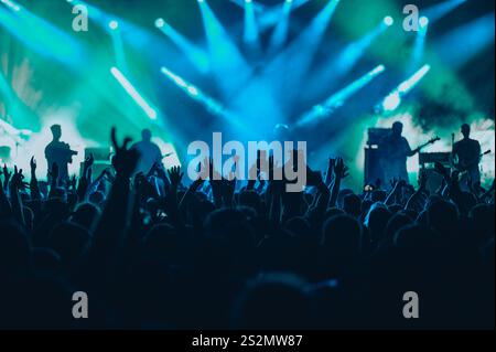 Eine große Gruppe von Leuten in einer Konzertgruppe, die abends Live-Auftritte auf einem Musikfestival genießen. Das Publikum hebt die Hände nach oben. Stockfoto