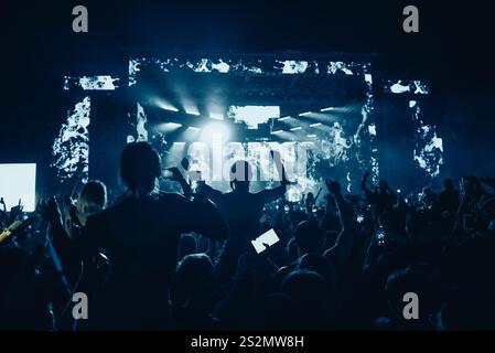 Jubelnde Menschenmenge vor hellen bunten Bühnenlichtern mit erhobenen Händen in der Luft und genießen das Konzert. Menschenmenge mit erhobenen Händen. Silhouetten. Stockfoto