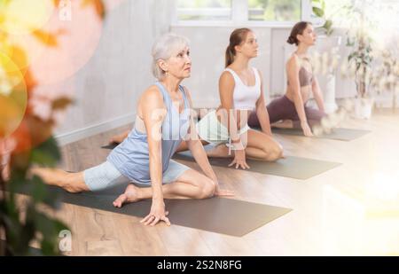 Ältere Frau dehnt sich in sitzender Asana Ardha Kapotasana im Yoga-Studio Stockfoto