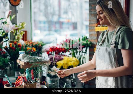 Floristin kreiert einen wunderschönen Blumenstrauß aus gemischten Blumen, während sie in einem Blumenladen arbeitet. Frau, die einen schönen Blumenstrauß auf der Co kreiert Stockfoto