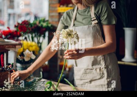 Floristin kreiert einen wunderschönen Blumenstrauß aus gemischten Blumen, während sie in einem Blumenladen arbeitet. Frau, die einen schönen Blumenstrauß auf der Co kreiert Stockfoto