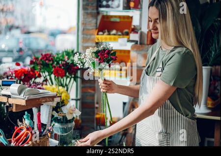 Floristin kreiert einen wunderschönen Blumenstrauß aus gemischten Blumen, während sie in einem Blumenladen arbeitet. Frau, die einen schönen Blumenstrauß auf der Co kreiert Stockfoto