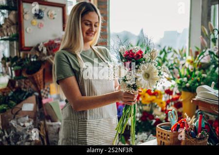 Floristin kreiert einen wunderschönen Blumenstrauß aus gemischten Blumen, während sie in einem Blumenladen arbeitet. Frau, die einen schönen Blumenstrauß auf der Co kreiert Stockfoto