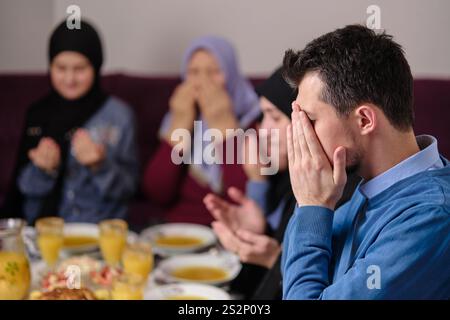 Die muslimische Familie macht iftar dua dazu, das Fasten während des Ramadan Esstisch zu Hause zu brechen, zusammen mit erhobenen Händen betend. Stockfoto