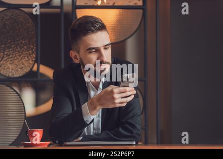 Porträt eines jungen glücklichen Geschäftsmannes, der an seinem Schreibtisch im Büro sitzt und ein Telefon benutzt. Stockfoto