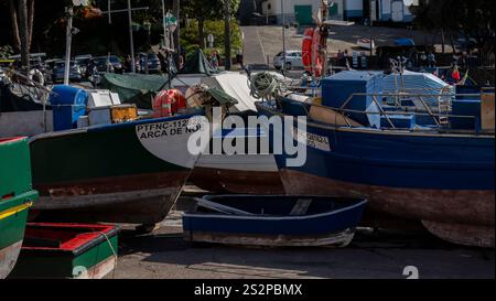 Eine Gruppe farbenfroher Fischerboote legte an Land an einem Yachthafen an, mit kleinen Holzbooten und maritimer Ausrüstung im Vordergrund. Stockfoto