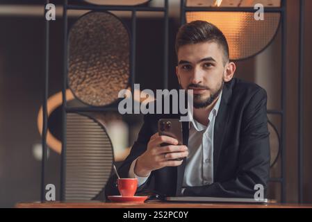 Porträt eines jungen glücklichen Mannes, der an seinem Schreibtisch im Büro sitzt und ein Telefon benutzt. Stockfoto