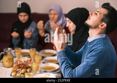 Die muslimische Familie macht iftar dua dazu, das Fasten während des Ramadan Esstisch zu Hause zu brechen, zusammen mit erhobenen Händen betend. Stockfoto
