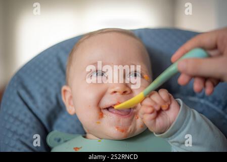 Glückliches 6 Monate altes Baby, das feste Nahrung mit Kombifütterung anfängt Stockfoto