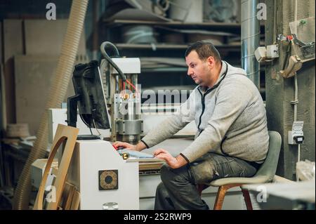 Industriearbeiter, der cnc-Bohrmaschinen in der Holzbearbeitungsindustrie bedient. Staubige Werkstatt und Möbelfabrik Konzept. Computer-Nr. Stockfoto