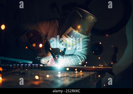 Junger Schweißer, der Bauhandschuhe und Schweißmaske trägt, harte Arbeit und Schweißen mit Schweißmaschine Metall in der Werkstatt. Kopierbereich. Porträt von Stockfoto