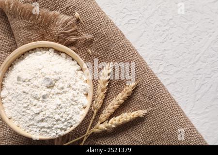 Schüssel mit Weizenmehl, Spikelets und Sackleinen auf hellem Hintergrund Stockfoto