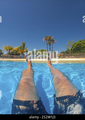 Die Beine eines Touristen schwimmen und sich während des Sommerurlaubs in einem Swimmingpool in einem Wasserpark entspannen Stockfoto