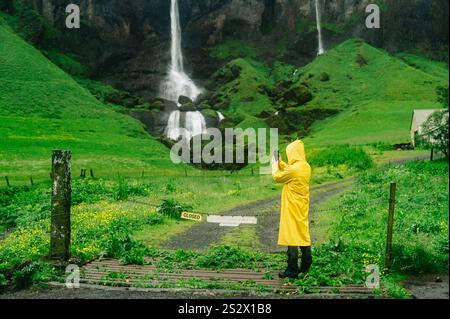 Ein Entdecker im Regenmantel steht in Island in der Natur und genießt die Wildnis. Ein Mann fotografiert einen Wasserfall in der wilden Natur Islands. Stockfoto