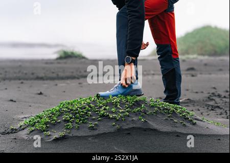 Nahaufnahme eines Läufers, der seinen Sneaker anpasst, während er am Meer in der wilden Natur Islands steht. Ein Sportler bereitet sich auf das Laufen in na vor Stockfoto