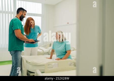 Ein medizinisches Team, bestehend aus einem Arzt und einer Ärztin, bespricht einen Behandlungsplan mit einer Patientin, die auf einem Krankenhausbett sitzt, in einem gut beleuchteten Kreise Stockfoto