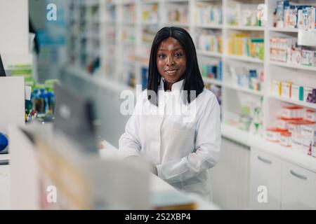 Porträt einer professionellen multikulturellen Apothekenarbeiterin im Labormantel, die an der Theke in Drogeriemärkten steht und Medikamente verkauft, während sm Stockfoto